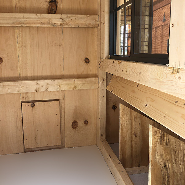 wooden interior showing nesting boxes and closed chicken door with glass board floor